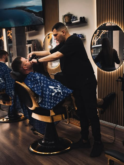 A barber grooming a client in the warm, softly lit Luxurious Barber shop.