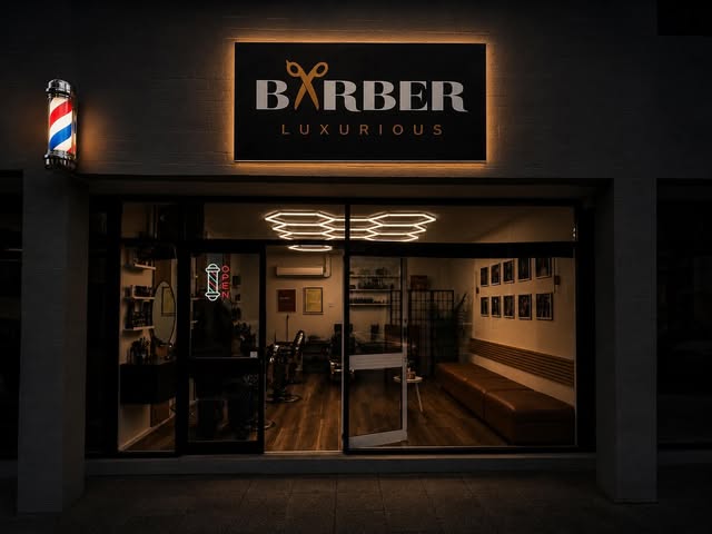 The illuminated Luxurious Barber shopfront at night.